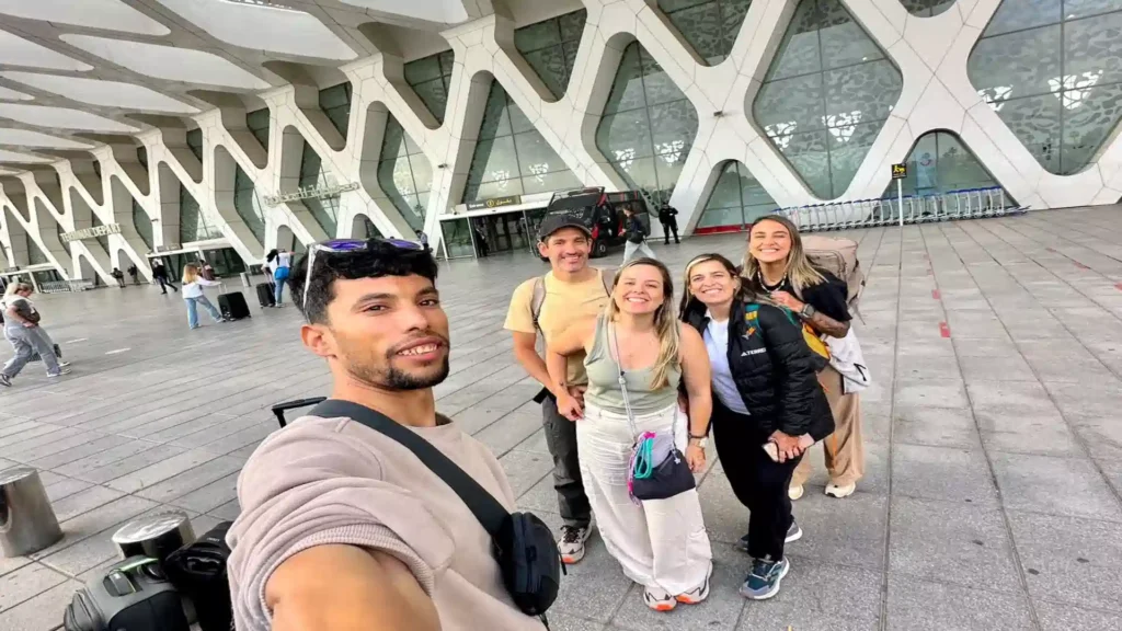 Local Moroccan tour guide taking a selfie with arriving travelers outside Marrakech Menara Airport with modern lattice architecture.that booked our 10 day morocco tour from Marrakech