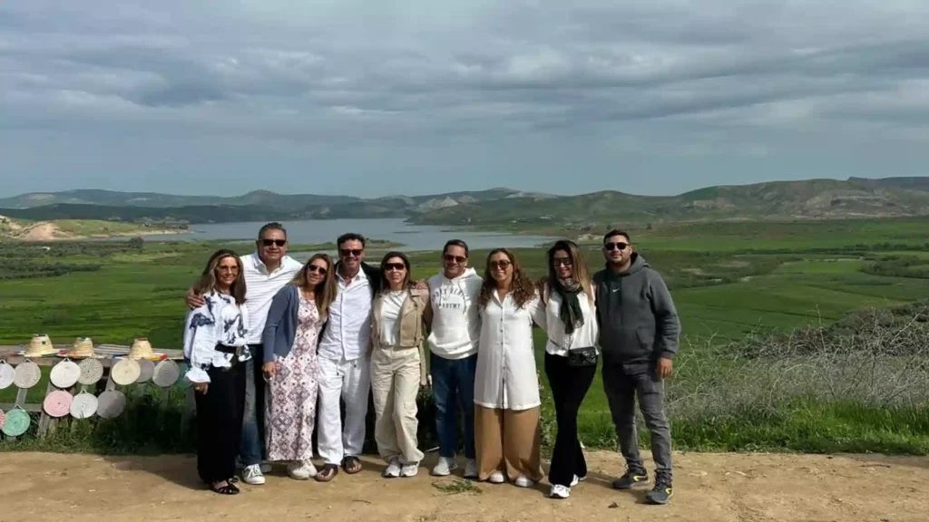 Group of happy travelers standing at a scenic viewpoint overlooking lush green hills and a peaceful lake in northern Morocco.
