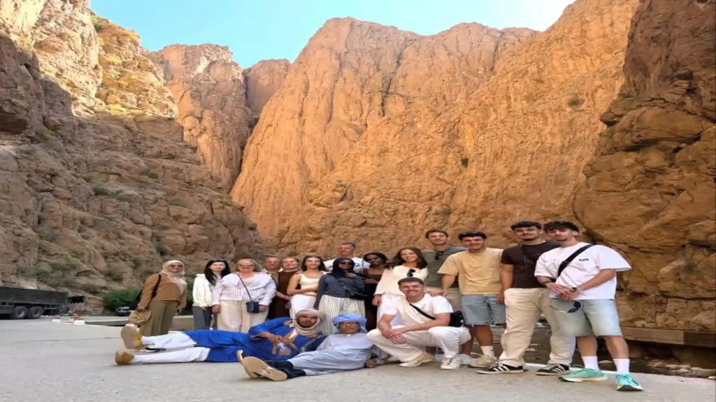 A group of cheerful travelers posing together on a golden sand dune in Merzouga during a Morocco desert tour from Casablanca.