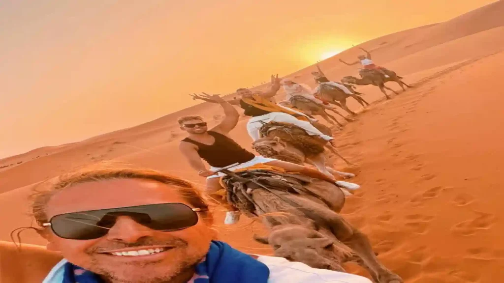 Happy travelers riding camels in a caravan during sunset in the Erg Chebbi desert dunes on a Morocco tour. morocco desert tour from Casablanca, 