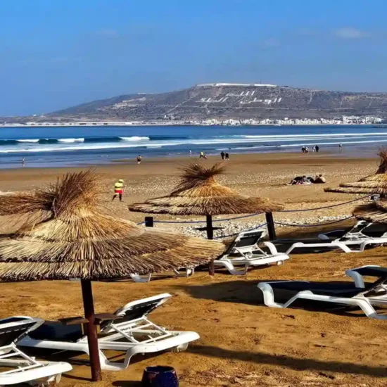 Agadir beach resort area with straw umbrellas and lounger chairs facing Agadir Oufella hill during a 12 days tour from Agadir to Marrakech