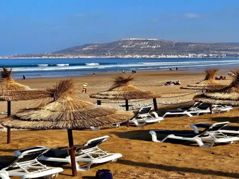 Agadir beach resort area with straw umbrellas and lounger chairs facing Agadir Oufella hill during a 12 days tour from Agadir to Marrakech