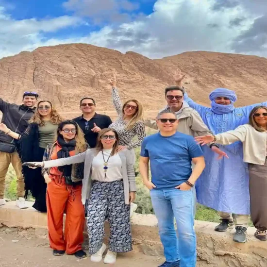 Happy group of travelers posing with a local guide at Todra Gorge palm oasis during a two weeks in Morocco itinerary