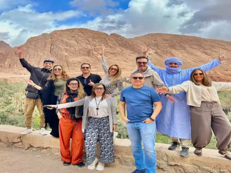 Happy group of travelers posing with a local guide at Todra Gorge palm oasis during a two weeks in Morocco itinerary
