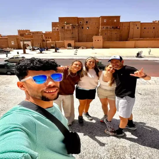 Happy travelers taking a group selfie in front of Kasbah Taourirt in Ouarzazate during a 10 days tour from Agadir Morocco