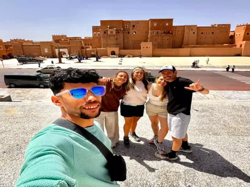 Happy travelers taking a group selfie in front of Kasbah Taourirt in Ouarzazate during a 10 days tour from Agadir Morocco