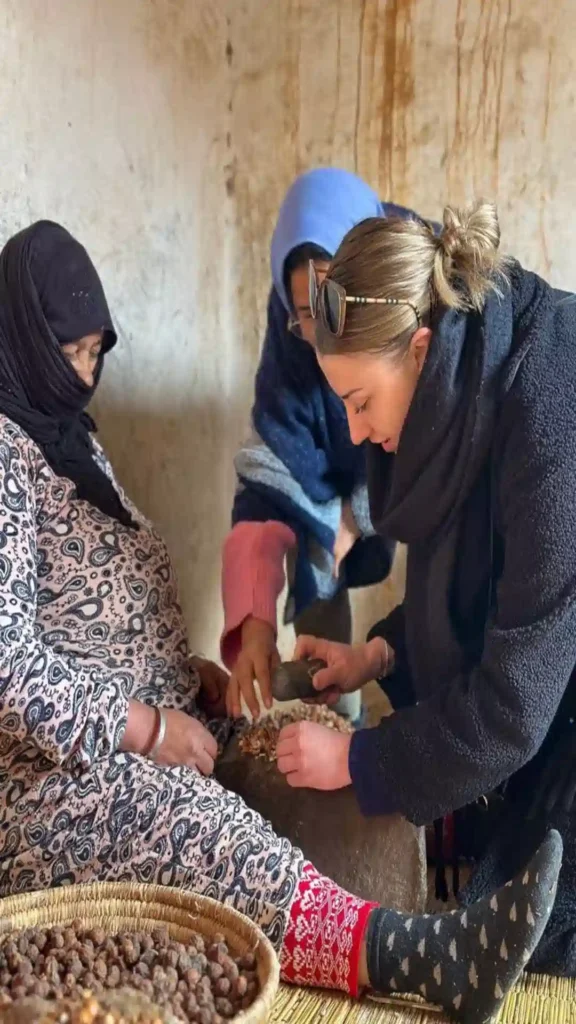 Moroccan argan Oil woman teaching visitor how to crack argan nuts using traditional stone tools
