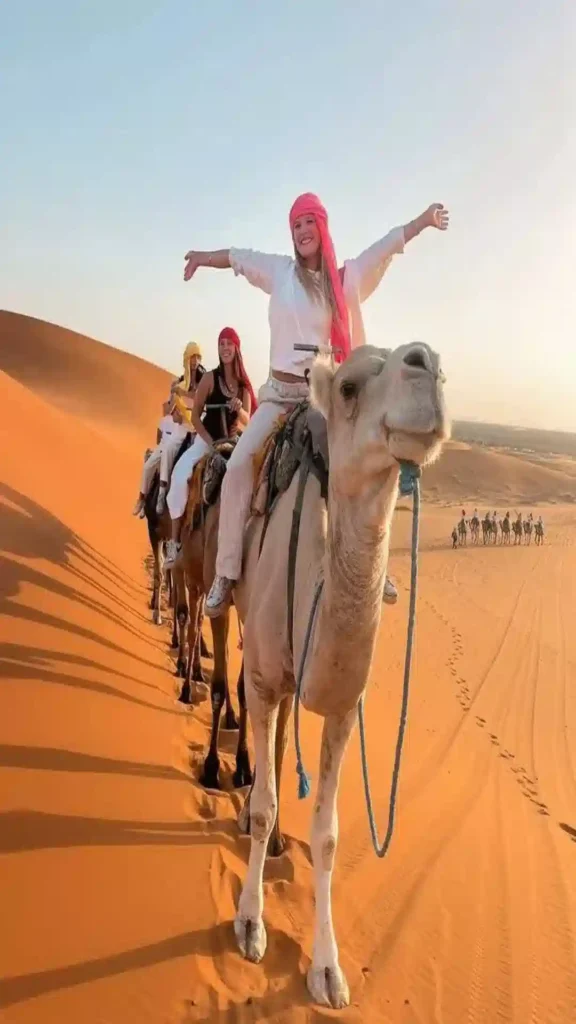 A caravan of travelers riding camels across high sand dunes in Erg Chebbi when planning what to do in Morocco.