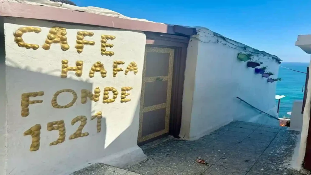 hite-washed exterior wall displaying gold lettering that reads Cafe Hafa Fonde 1921 with a view of the ocean in the background. best things to do in Tangier