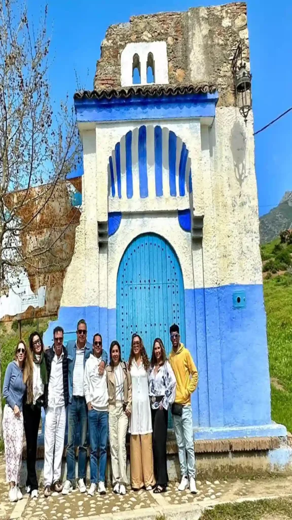 A group of tourists posing in front of the blue-and-white painted entrance arch of the Spanish Mosque overlooking Chefchaouen, Morocco.why is chefchaouen blue.