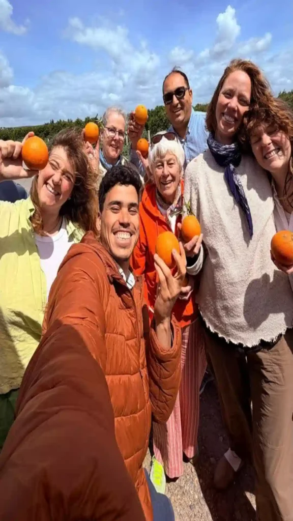 A happy group of travelers holding fresh oranges during an agricultural farm tour experience for what to do in Morocco.