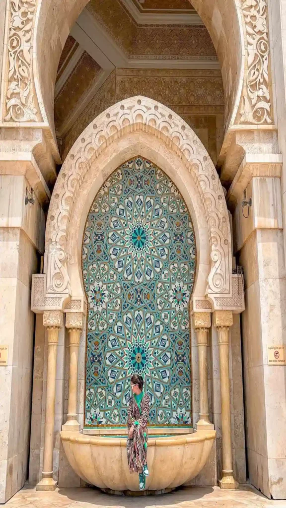 A traveler sitting on the marble rim of an intricate zellige tiled wall fountain while discovering what to do in Morocco.