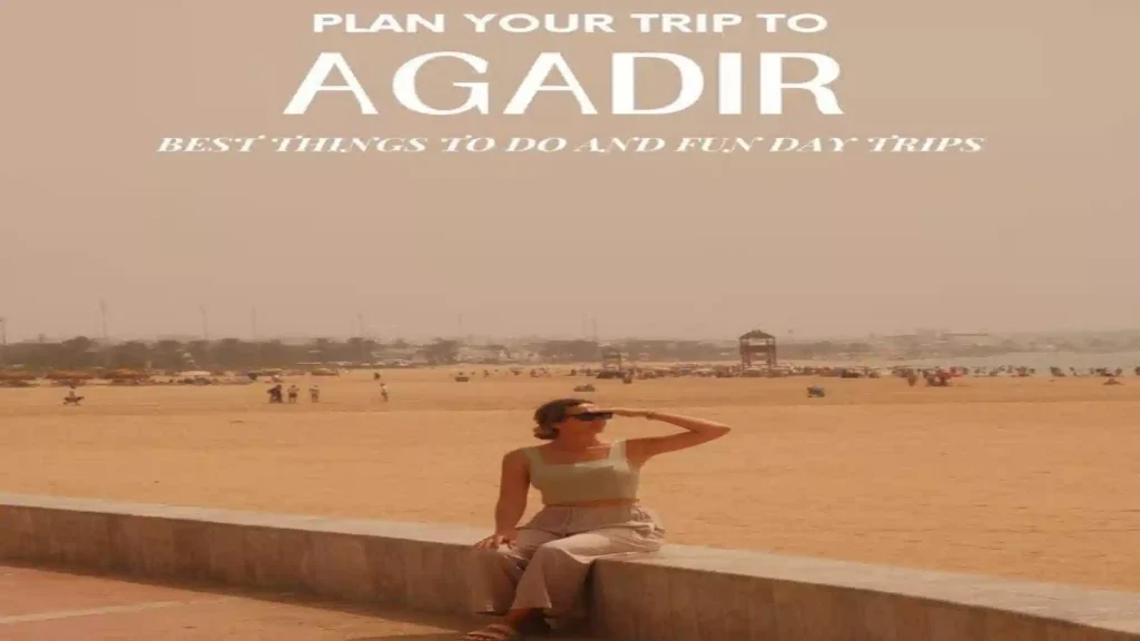 A woman in sunglasses sitting on the sea wall along the sandy Agadir beach promenade with title text reading Plan Your Trip to Agadir. things to do in Agadir Morocco