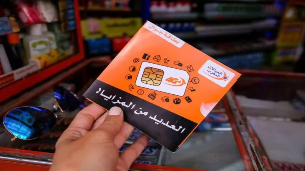 A person holding an orange Maroc Telecom 4G prepaid SIM card package above a store counter. Morocco eSIM