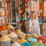A traveler selecting spices from open baskets in a colorful medina shop with shelves packed in every corner.Is Marrakech Worth Visiting
