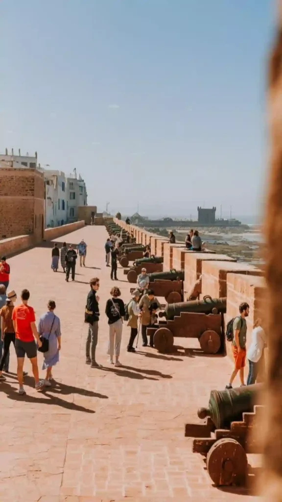Tourists exploring the Skala de la Kasbah ramparts in Essaouira, lined with historic bronze cannons facing the sea. things to do in Essaouira Morocco.