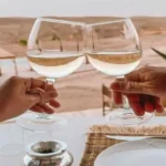 Two wine glasses clinking together with a luxury desert resort and pool in the background during luxury travel Morocco.