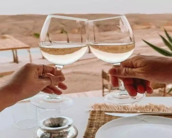 Two wine glasses clinking together with a luxury desert resort and pool in the background during luxury travel Morocco.