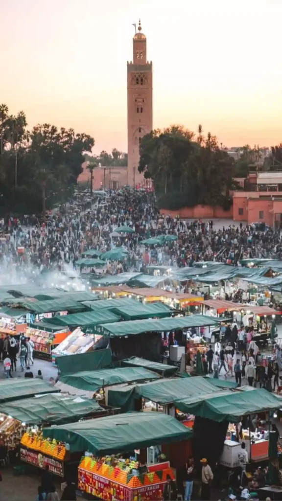 High-angle view of Jemaa el-Fna square filled with food stalls, crowds, and the Koutoubia Mosque minaret in every corner.