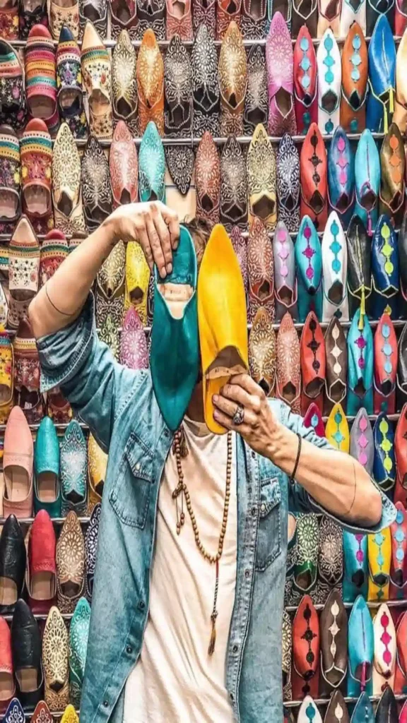 Person holding teal and yellow leather babouche slippers against a wall of colorful shoes in the 7 best souks in Marrakech.