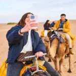 A woman taking a selfie with her smartphone while riding a camel across the Sahara desert in Morocco eSIM.