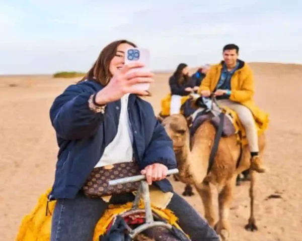 A woman taking a selfie with her smartphone while riding a camel across the Sahara desert in Morocco eSIM.