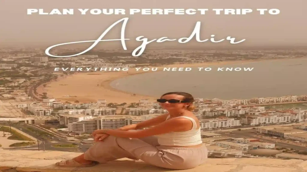 A traveler sitting on the stone wall at Agadir Oufella overlooking the city skyline and crescent bay.things to do in Agadir Morocco