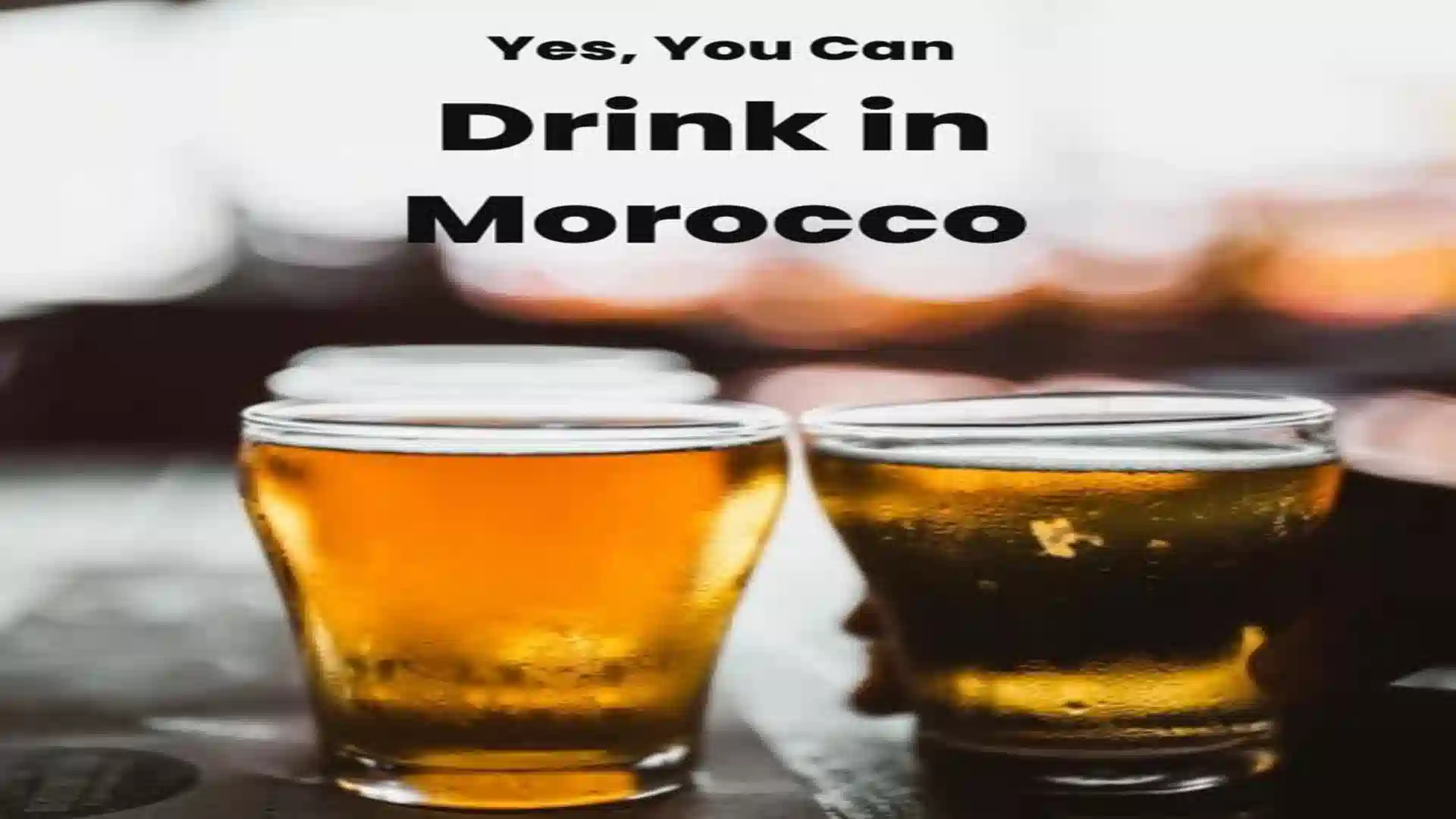 A Pinterest graphic with bold text overlay reading "Yes, You Can Drink in Morocco" above two blurred glasses of draft beer. alcohol in Morocco.